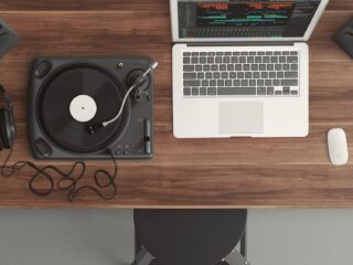 A top view of a turntable and a laptop on a wooden table, with headphones and a speaker in the background.