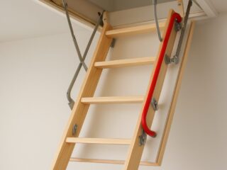 Close-up of a wooden loft ladder with a red handrail