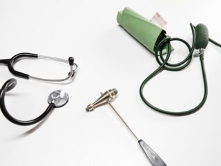 Medical instruments including a stethoscope, reflex hammer, and sphygmomanometer on a white surface